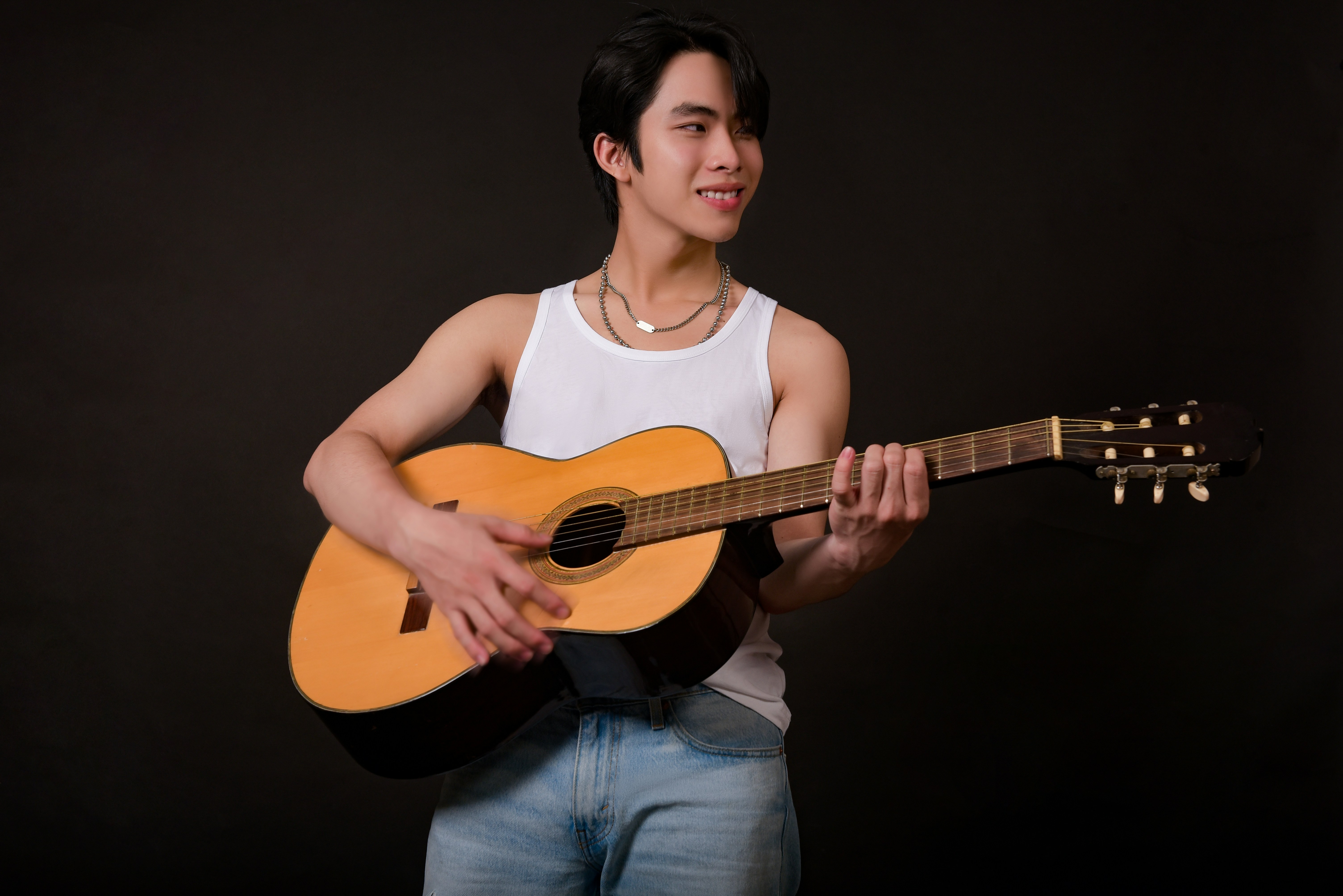 Wanita dengan tank top putih dan jeans denim biru memegang gitar akustik coklat