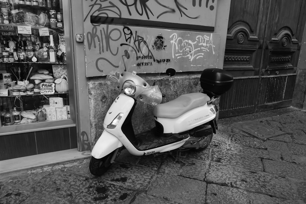 white and black motor scooter parked beside wall with graffiti
