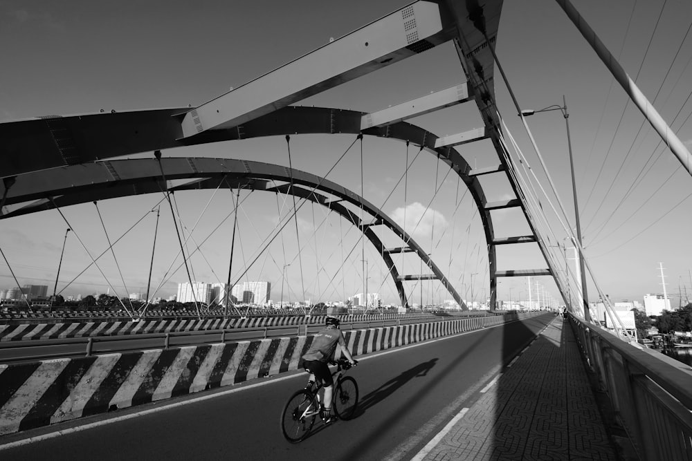 grayscale photo of person riding bicycle on bridge