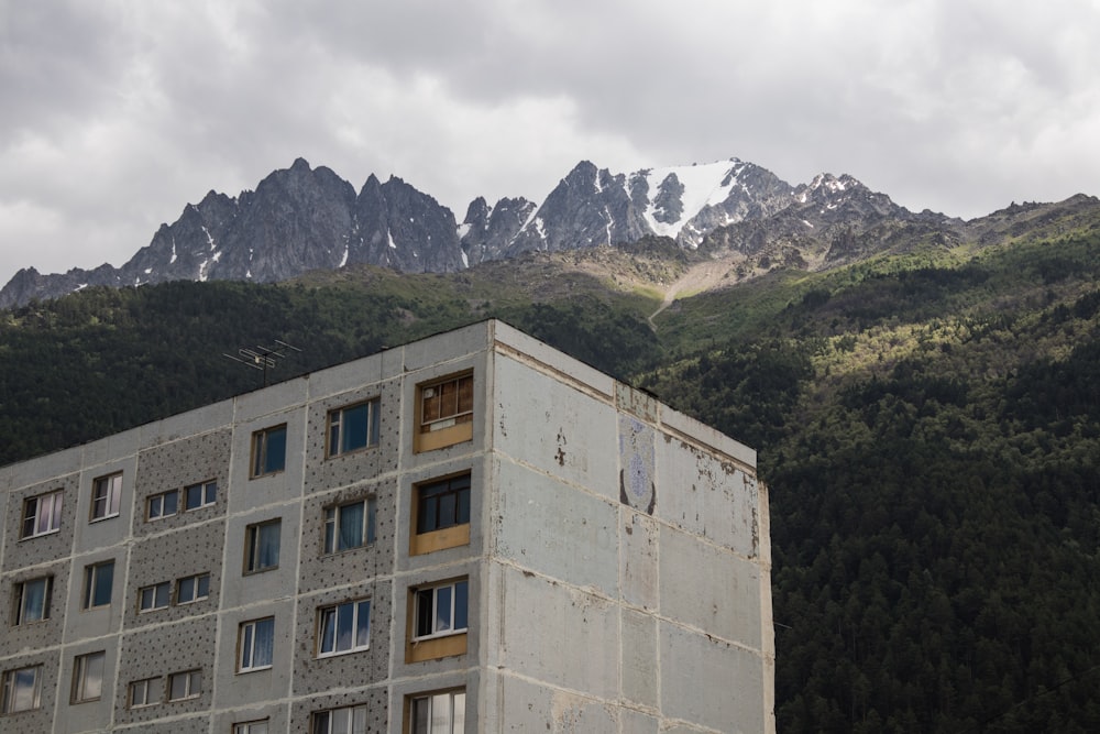 brown concrete building near green trees and mountain during daytime