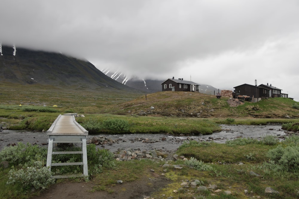 white wooden house on green grass field near mountain under white sky during daytime