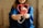 A person wearing a blue garment is holding a pink stethoscope shaped into a heart. The focus is on their hands and the stethoscope, suggesting a connection to healthcare or caring professions.