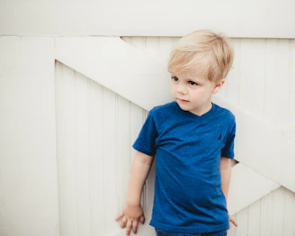 boy in blue crew neck t-shirt standing beside white wall