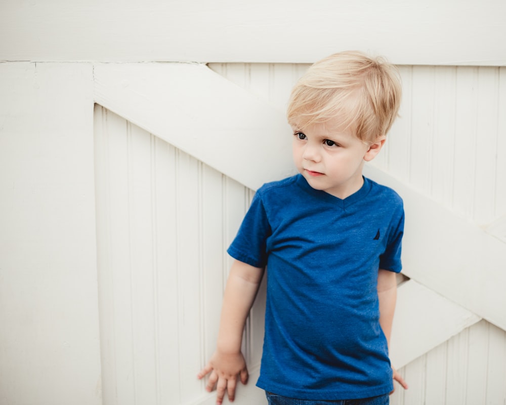 boy in blue crew neck t-shirt standing beside white wall