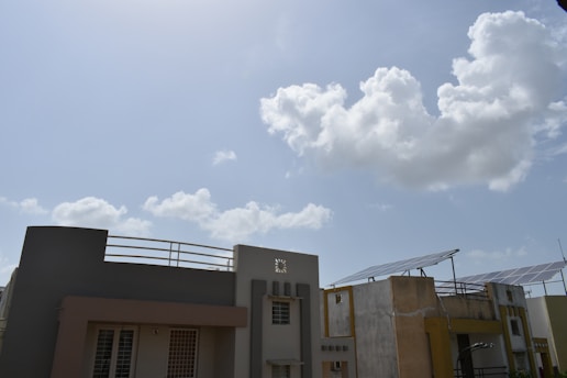 Modern buildings with flat rooftops featuring solar panels, set against a bright blue sky with fluffy white clouds.