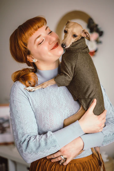 Mujer con sueter gris cargando a un perro cafe con sueter verde