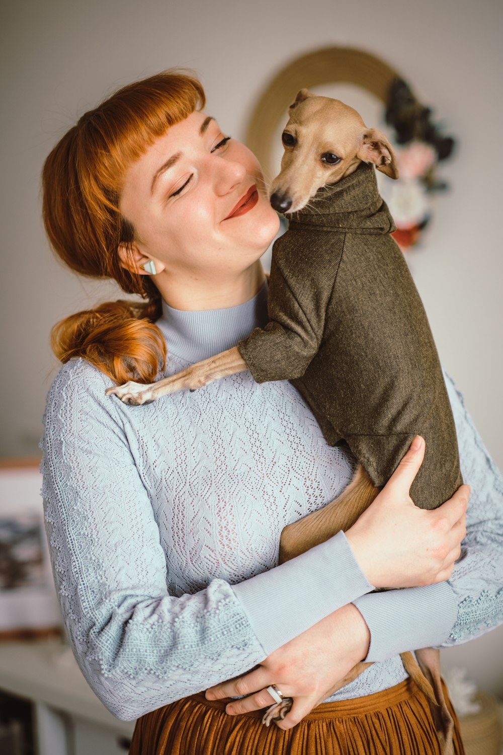 woman in gray sweater hugging brown short coated dog
