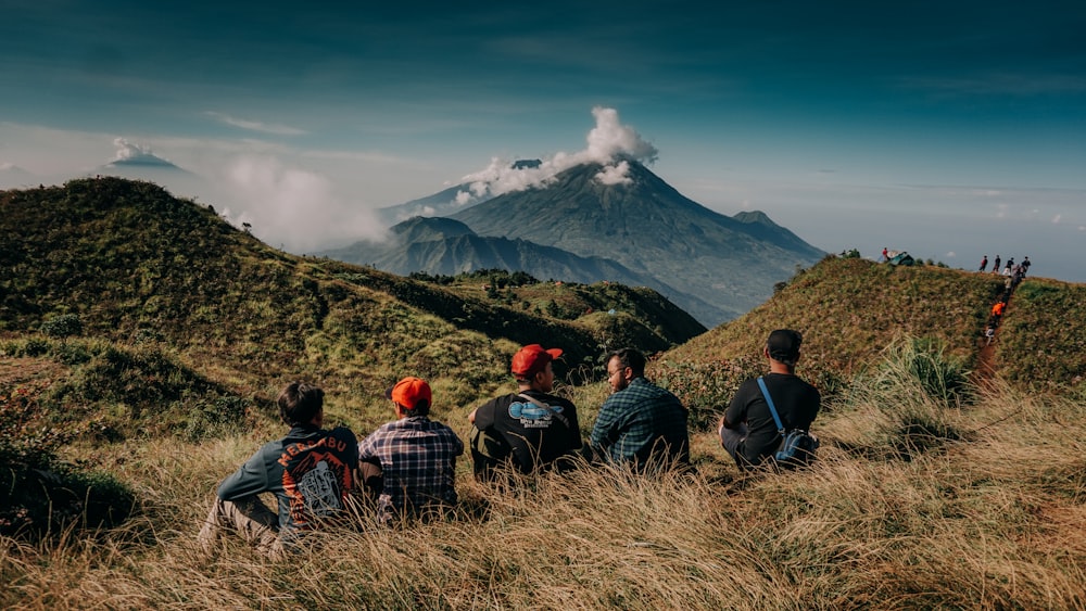 people sitting on grass field near mountain under blue sky during daytime