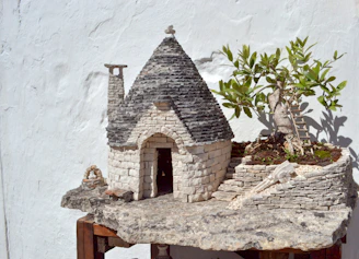 Close-up of a miniature house under construction with tiny tools and natural stone details.