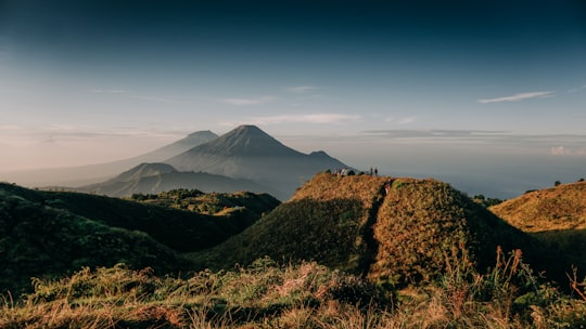 green grass field near mountain under blue sky during daytime in Gunung Prau Indonesia