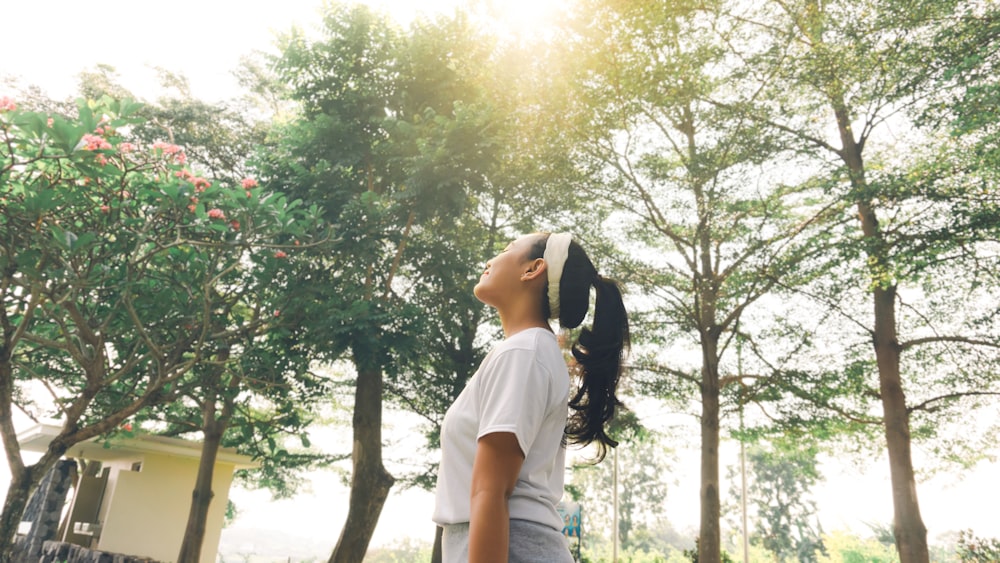 woman in white t-shirt and blue denim shorts standing under green tree during daytime