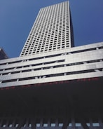 A tall skyscraper with a grid-like pattern of windows against a clear blue sky. The building is modern, with a silver and gray facade, and features an LED ticker displaying text in red.