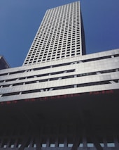 A tall skyscraper with a grid-like pattern of windows against a clear blue sky. The building is modern, with a silver and gray facade, and features an LED ticker displaying text in red.