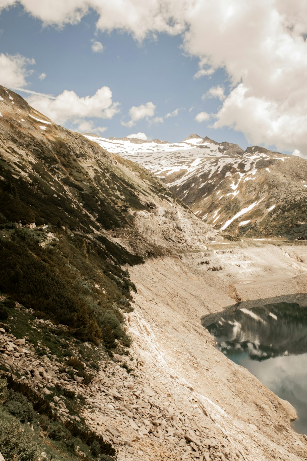 brown and white mountains near lake under white clouds and blue sky during daytime