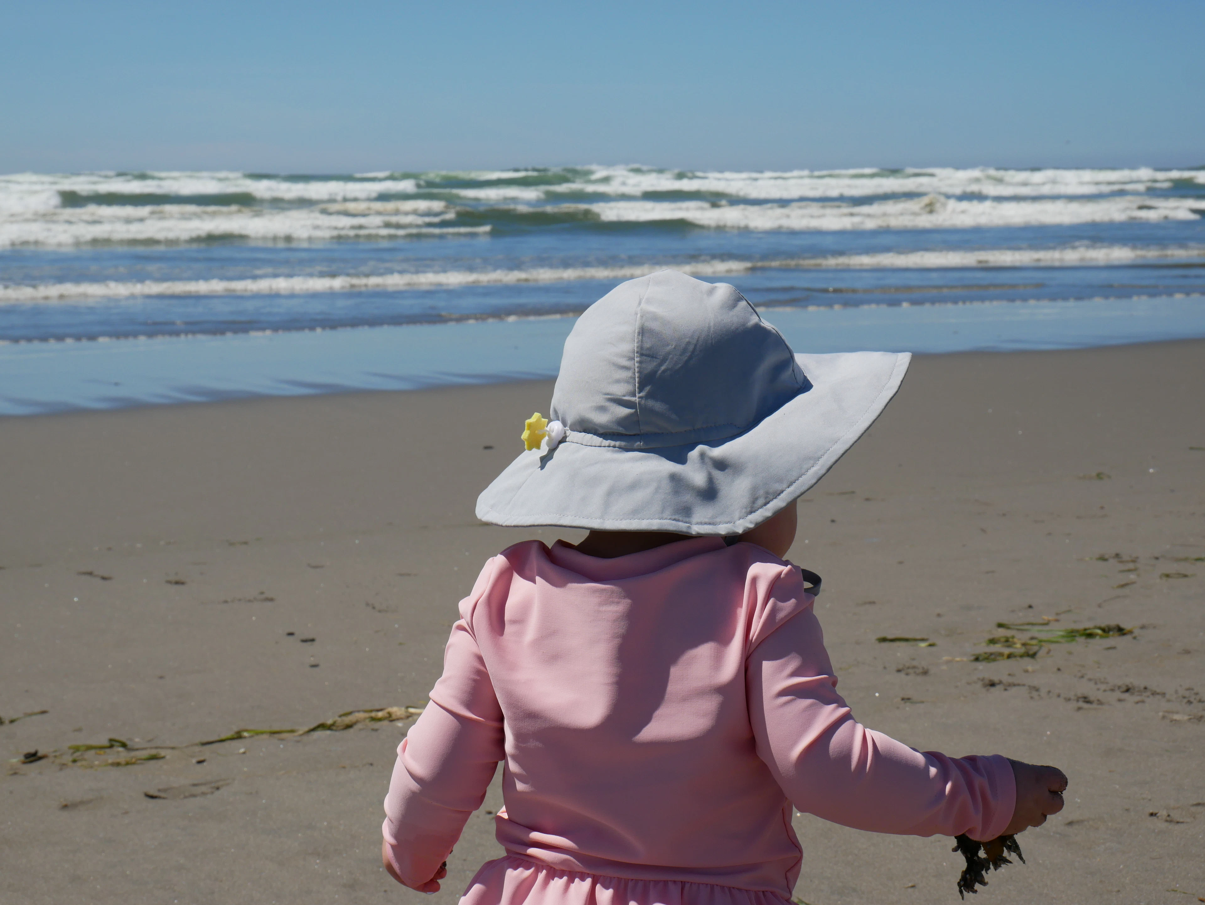 A toddler in a pink sun hoodie walking on the beach