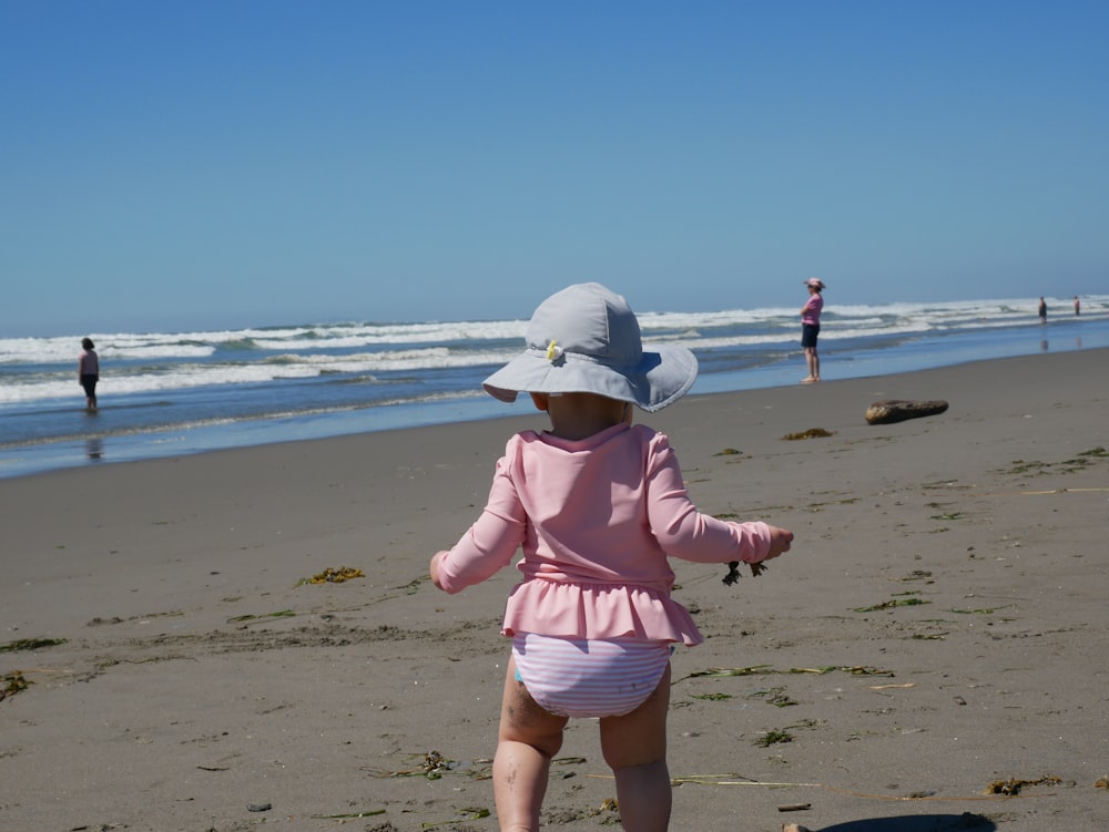 menina no vestido cor-de-rosa que anda na praia durante o dia