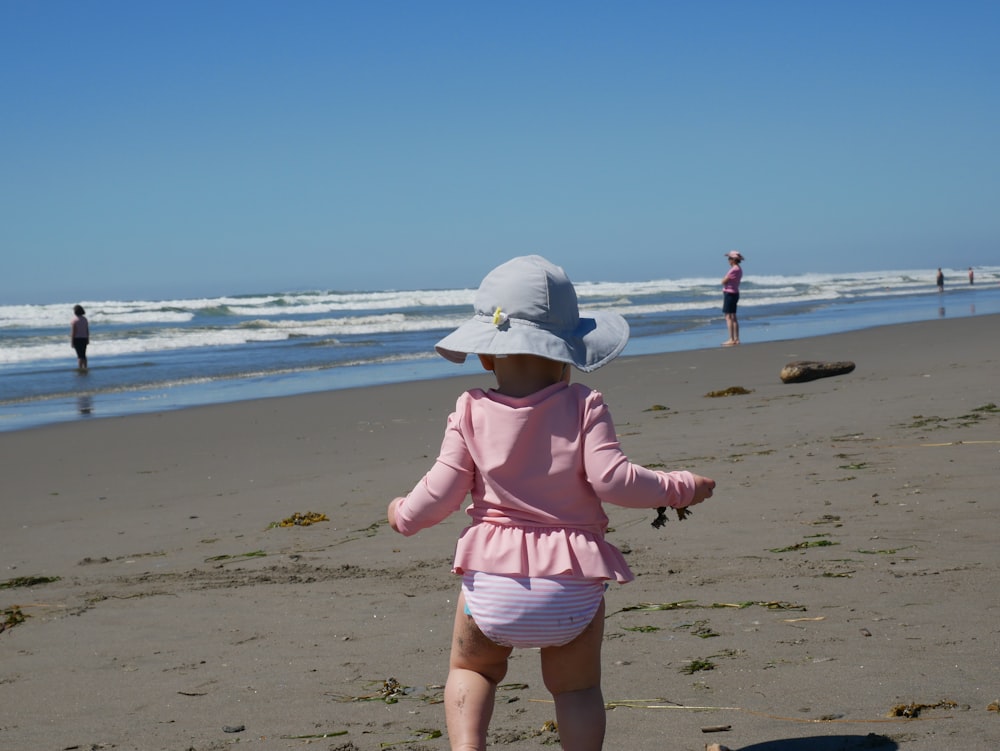 girl in pink dress walking on beach during daytime