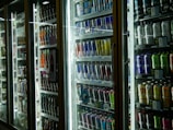 Brightly lit refrigerators filled with an assortment of beverages, including energy drinks, sodas, and juices, neatly arranged and displayed through glass doors.