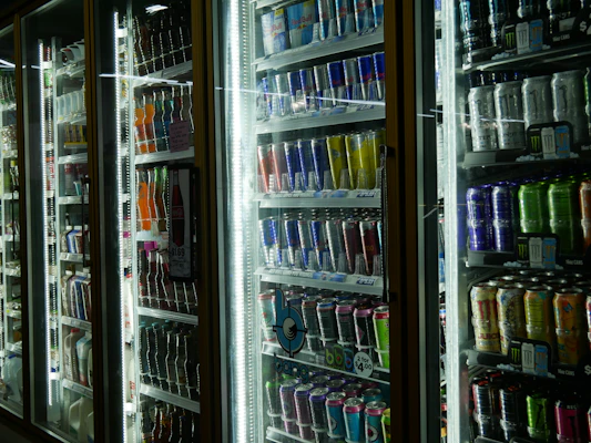 A variety of beverages including sodas and juices chilled in a glass-front refrigerator.