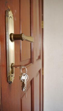 A wooden door with a brass handle and a set of keys dangling from the lock. The door appears sturdy with a slightly glossy finish, and the keys are attached to a simple keyring.
