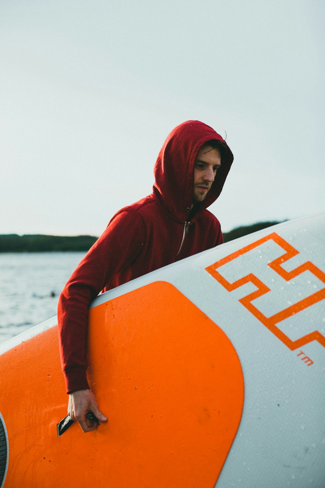 woman in red hoodie holding orange and white surfboard