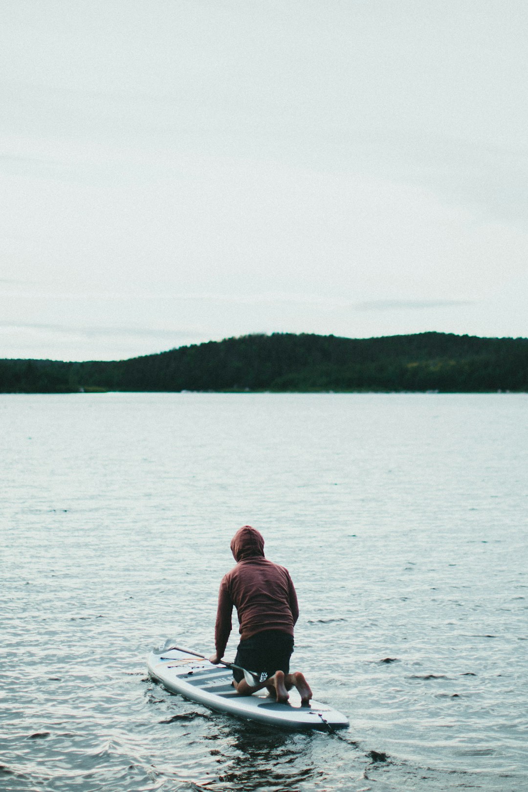 man in red hoodie sitting on boat on lake during daytime