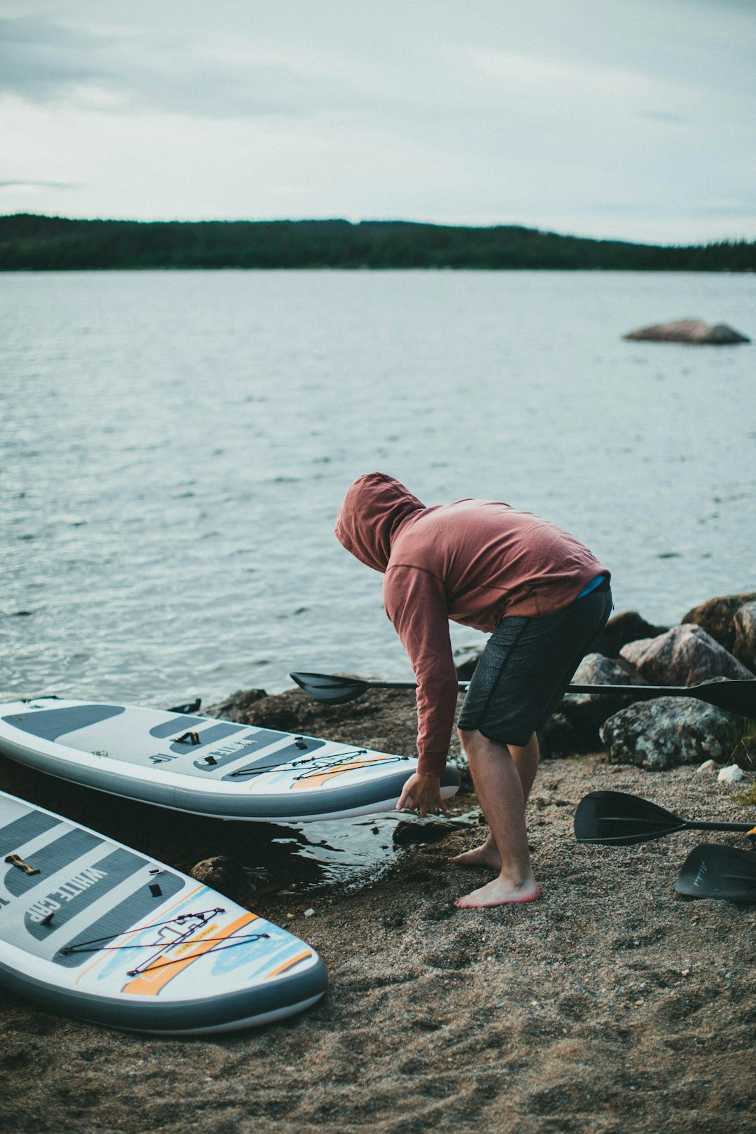 man in red hoodie and blue denim jeans standing on white and blue boat during daytime