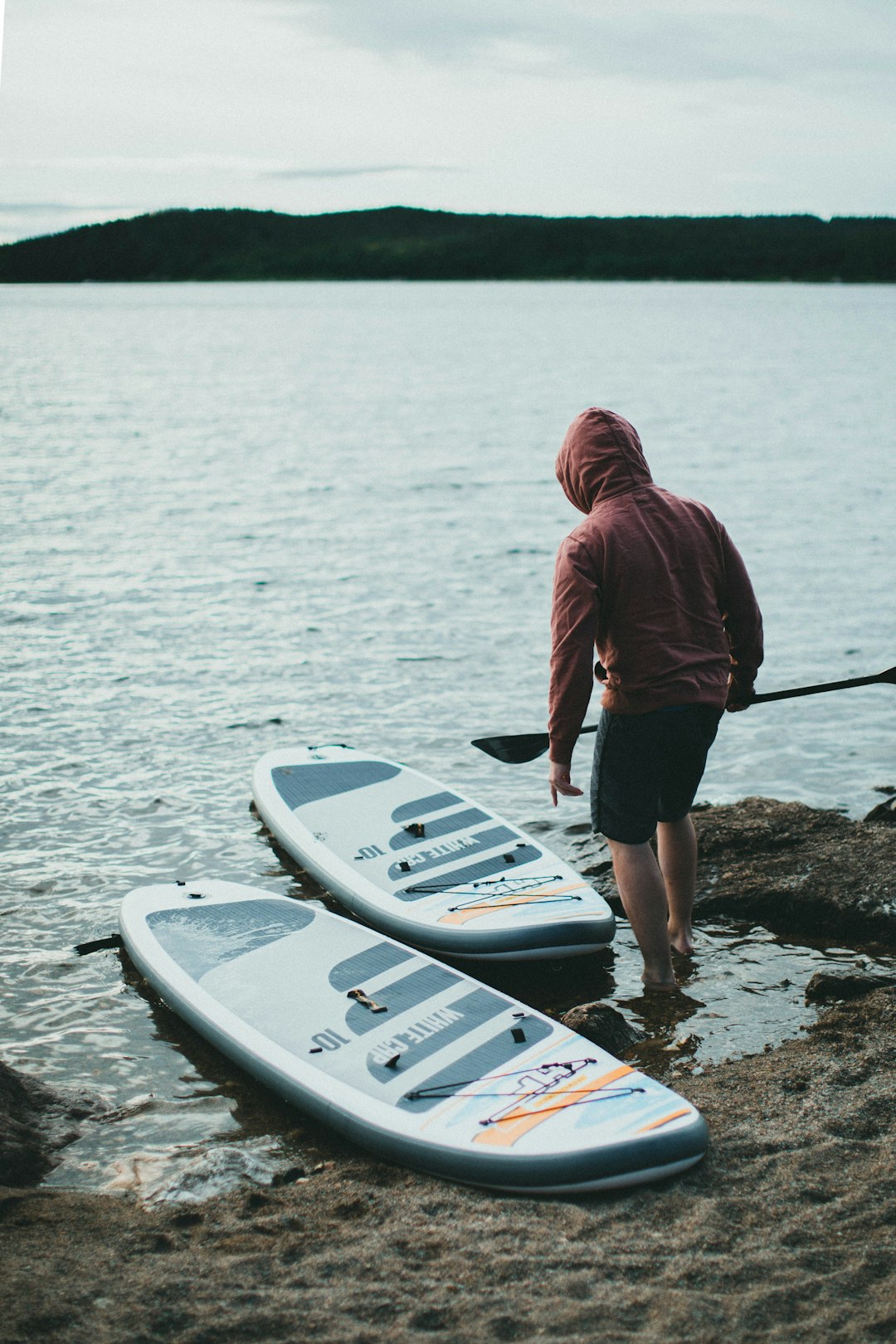man in red hoodie and black shorts standing on white surfboard on body of water during