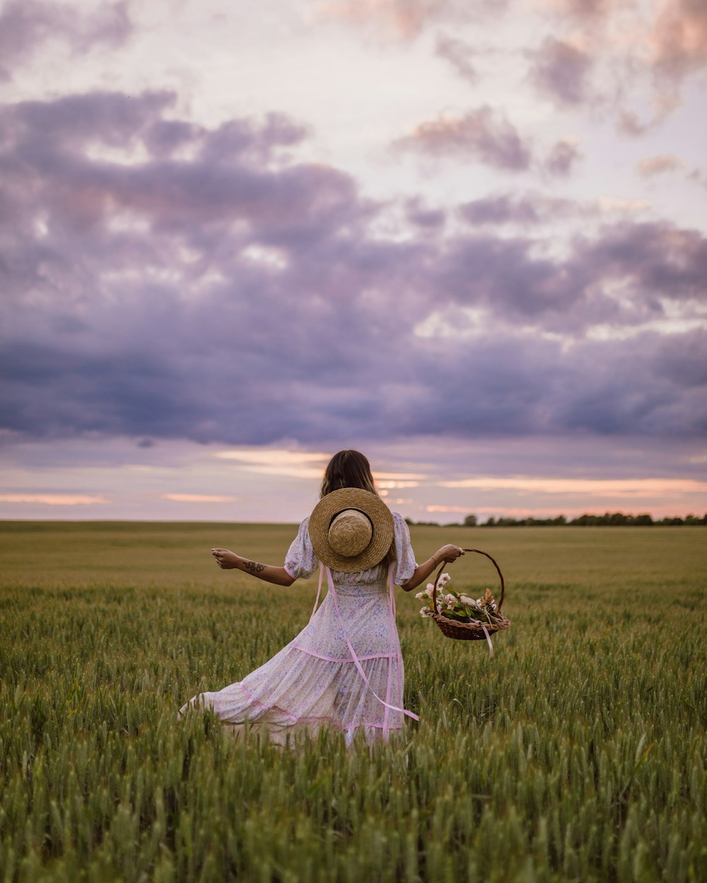 woman in white dress sitting on green grass field under cloudy sky during daytime