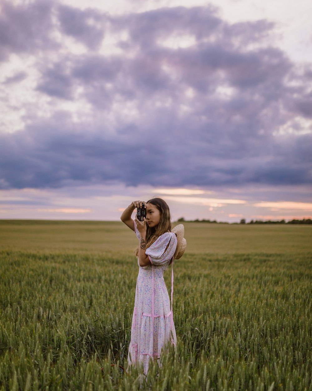 woman in white and pink dress standing on green grass field under cloudy sky during daytime