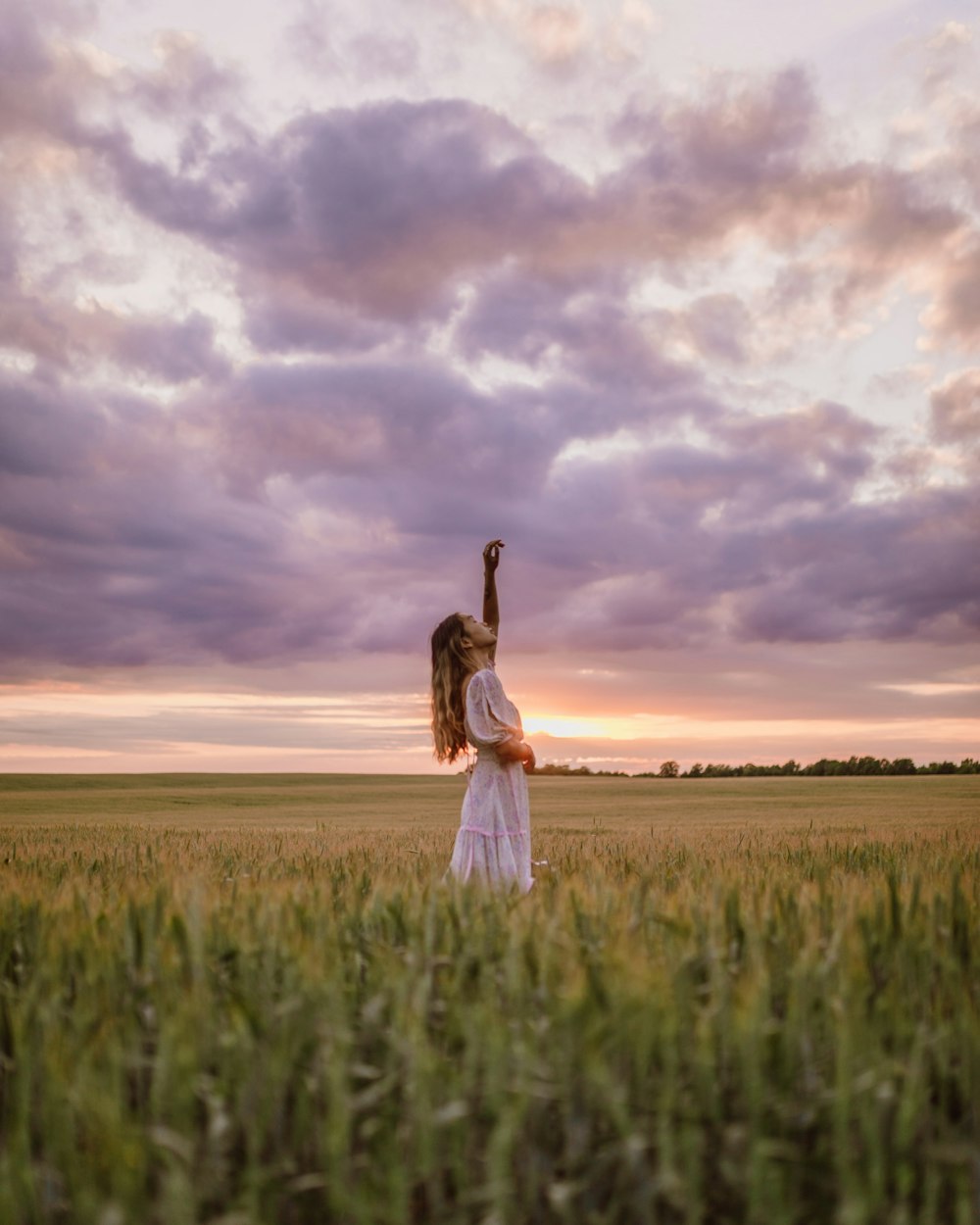 woman in white dress standing on green grass field under cloudy sky during daytime