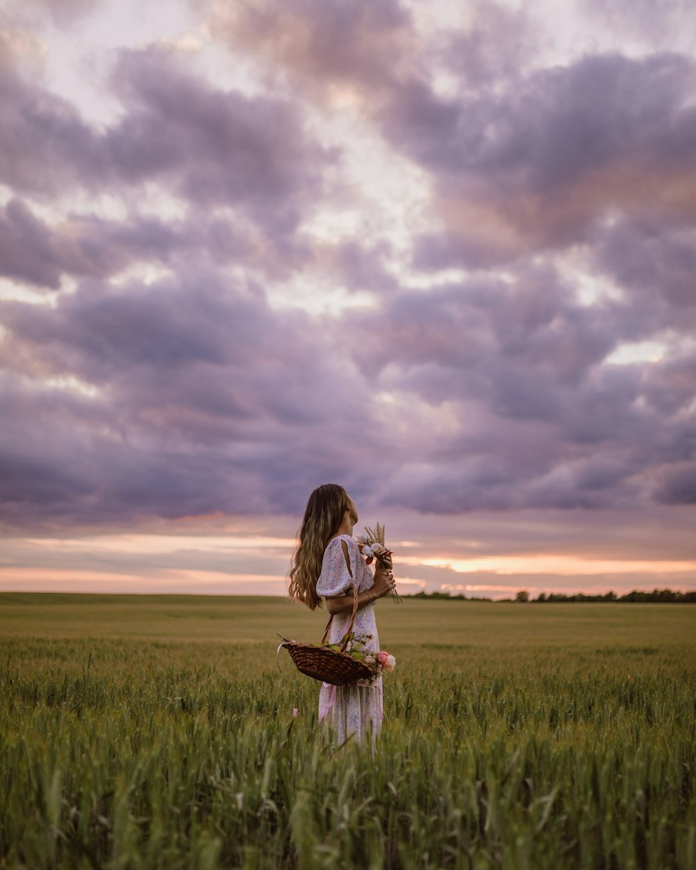 woman in white and black dress holding brown basket on green grass field under cloudy sky