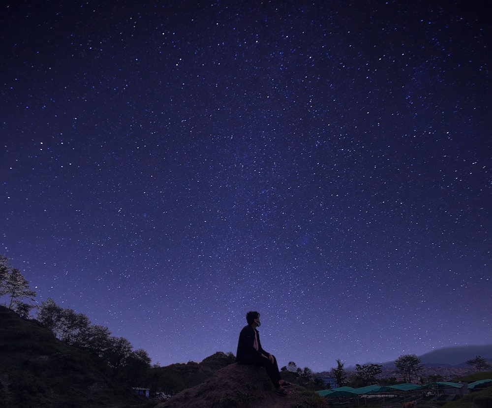 man in black jacket standing on rock under starry night