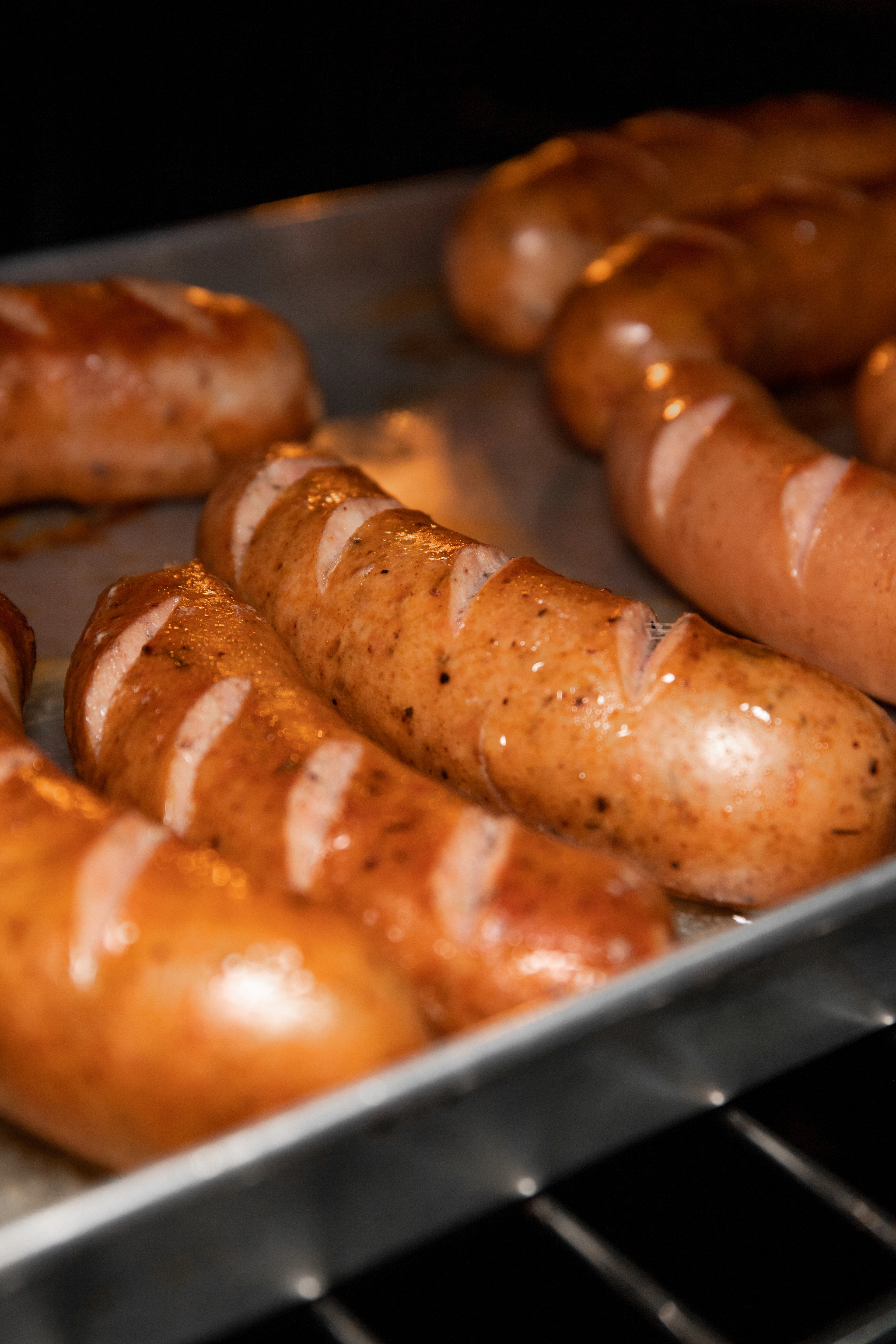 Grilled sausages browning on a tray, scored and glistening from the grill