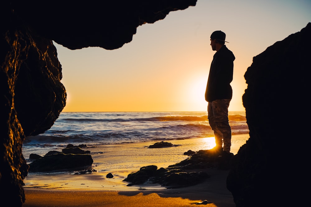 Silhouette von Mann und Frau, die während des Sonnenuntergangs am Strandufer stehen