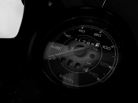 A close-up view of a speedometer displaying numbers in a range of 0 to 140 km/h. The needle is pointing slightly above 20 km/h. The odometer shows a reading of 21295.7 kilometers. The image is rendered in shades of black and white, which adds a dramatic and classic feel to the scene.