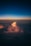 A vibrant cloud formation is illuminated by the warm hues of a sunset, contrasting against a deep blue sky above. The lighted clouds create a dramatic and serene atmosphere as they float over a darker landscape.