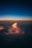 A vibrant cloud formation is illuminated by the warm hues of a sunset, contrasting against a deep blue sky above. The lighted clouds create a dramatic and serene atmosphere as they float over a darker landscape.