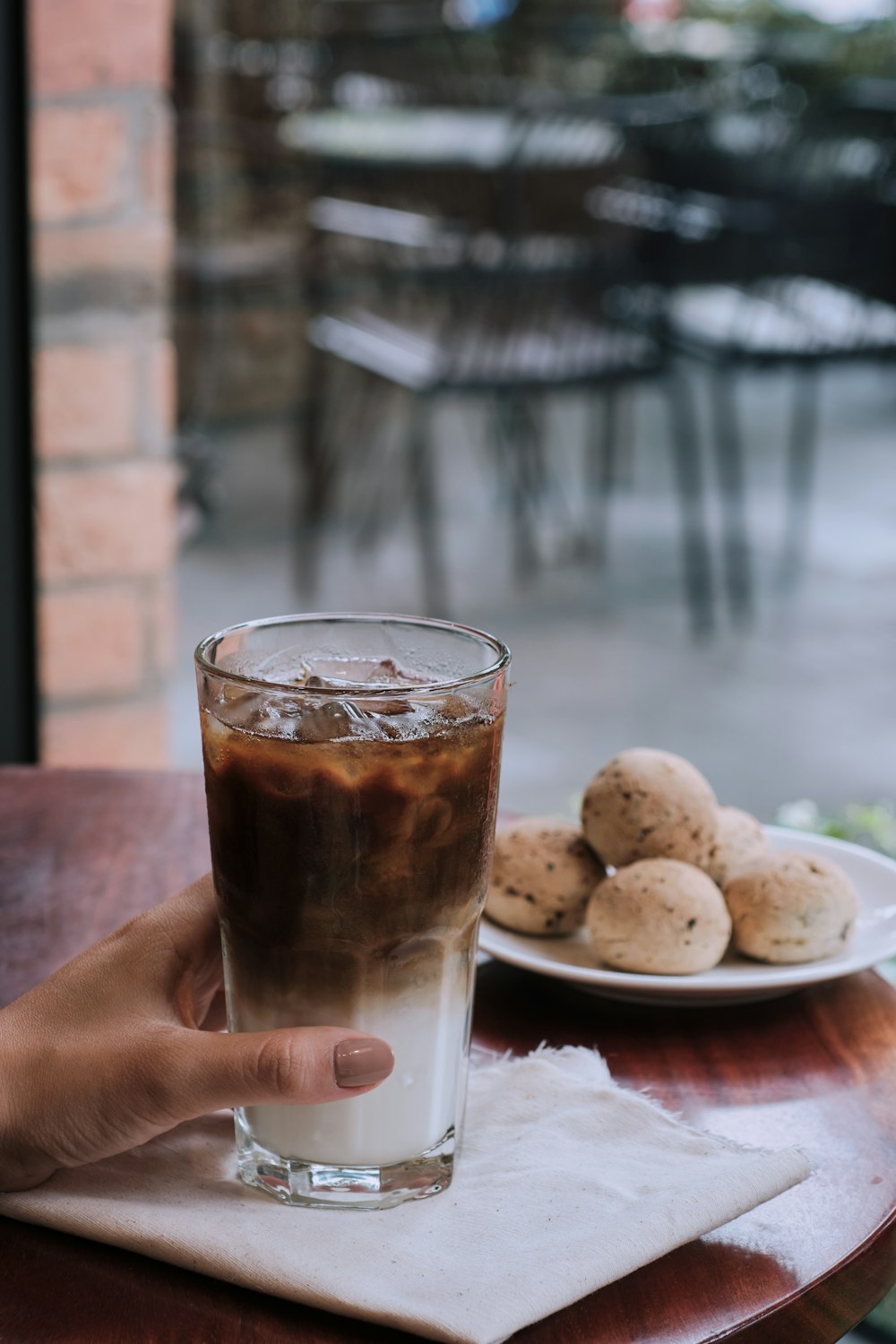 person holding clear drinking glass with brown liquid