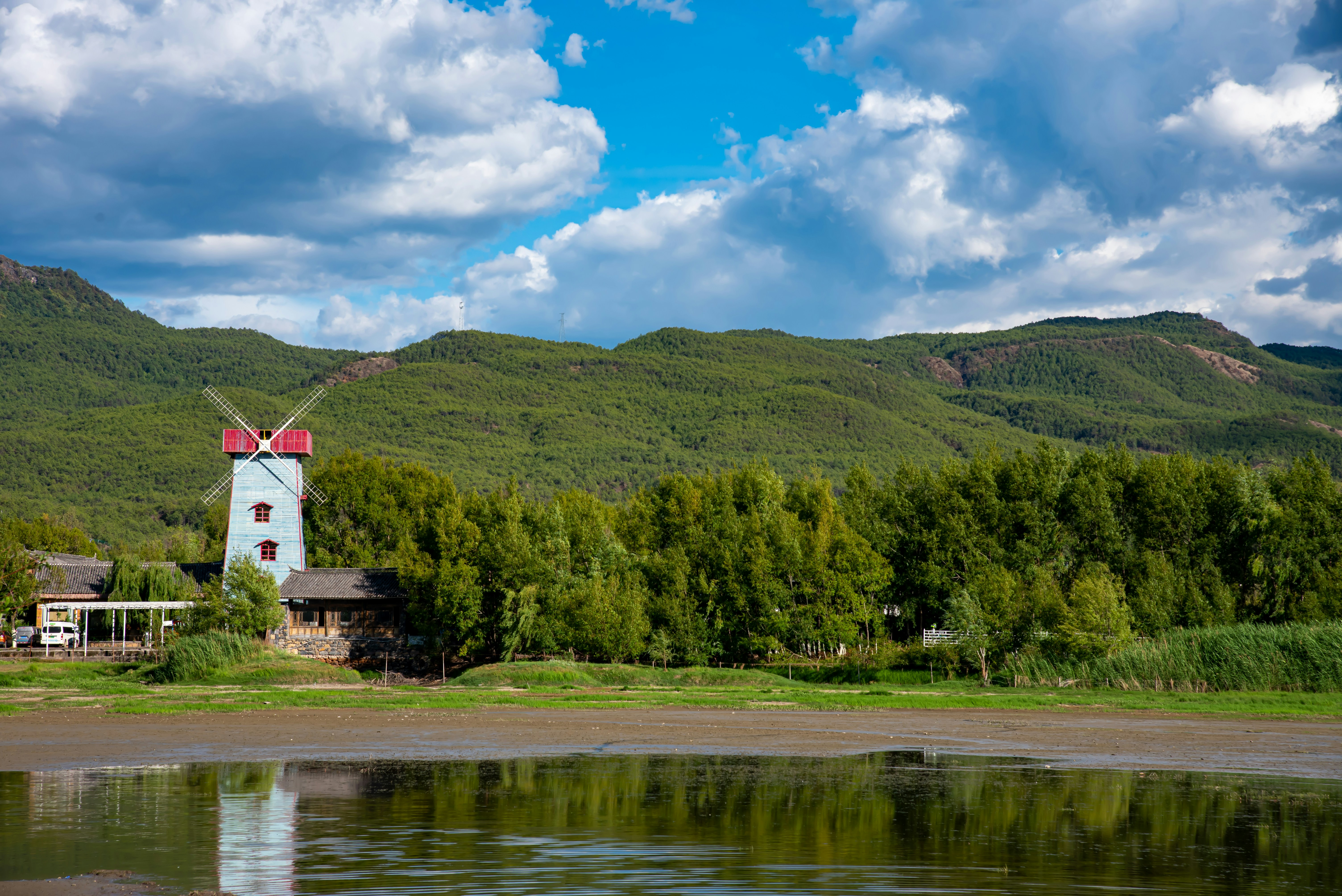 white and red house near green trees and lake under blue sky during daytime