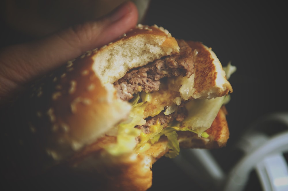 person holding burger with cheese