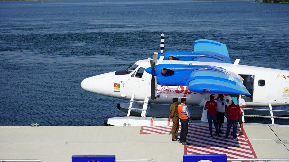 Persone che camminano sul molo vicino all'aeroplano bianco e blu durante il giorno