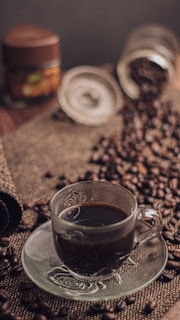 Freshly brewed coffee in a clear glass cup, surrounded by coffee beans and a cozy atmosphere.