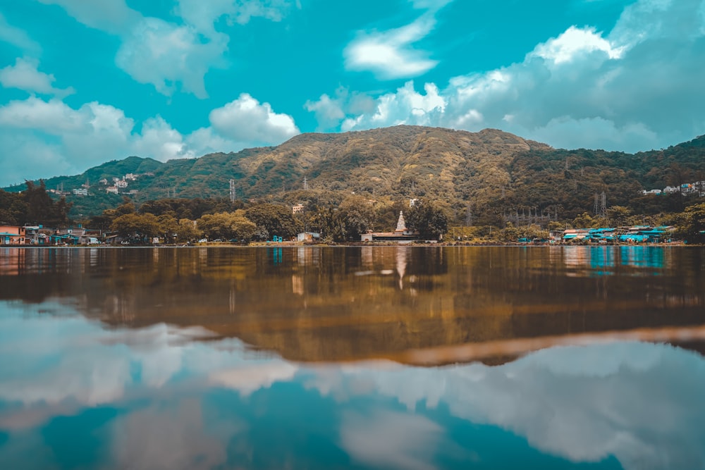 brown wooden dock on lake near green mountain under blue sky and white clouds during daytime