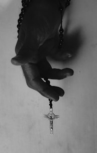 Hands holding a rosary against a backdrop of a stained-glass window depicting Our Lady of Victory.