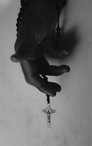 Hands holding a rosary over an open Bible with soft natural light.