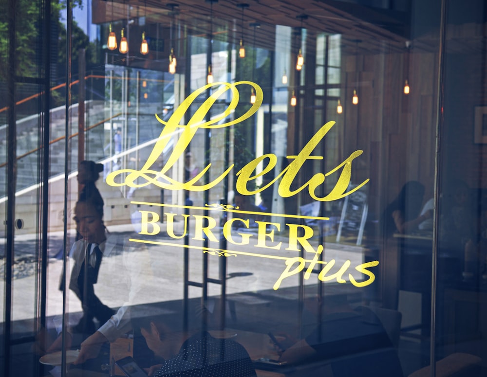 a woman walking past a glass window with the words lotus's burger plus on