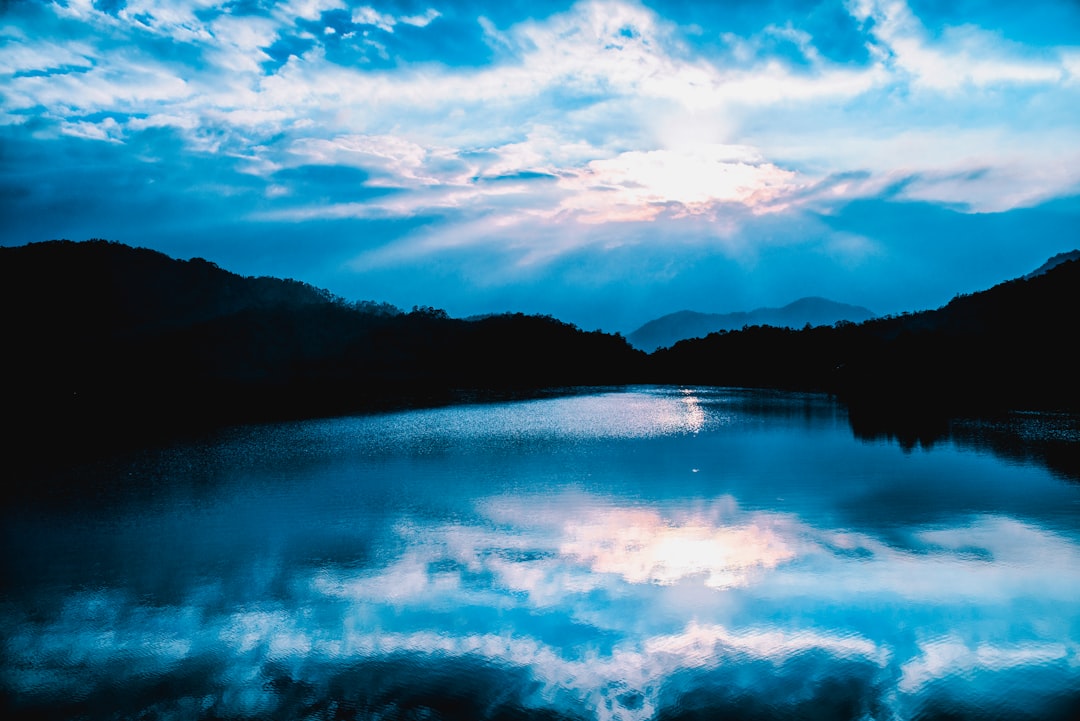 body of water near mountain under cloudy sky during daytime