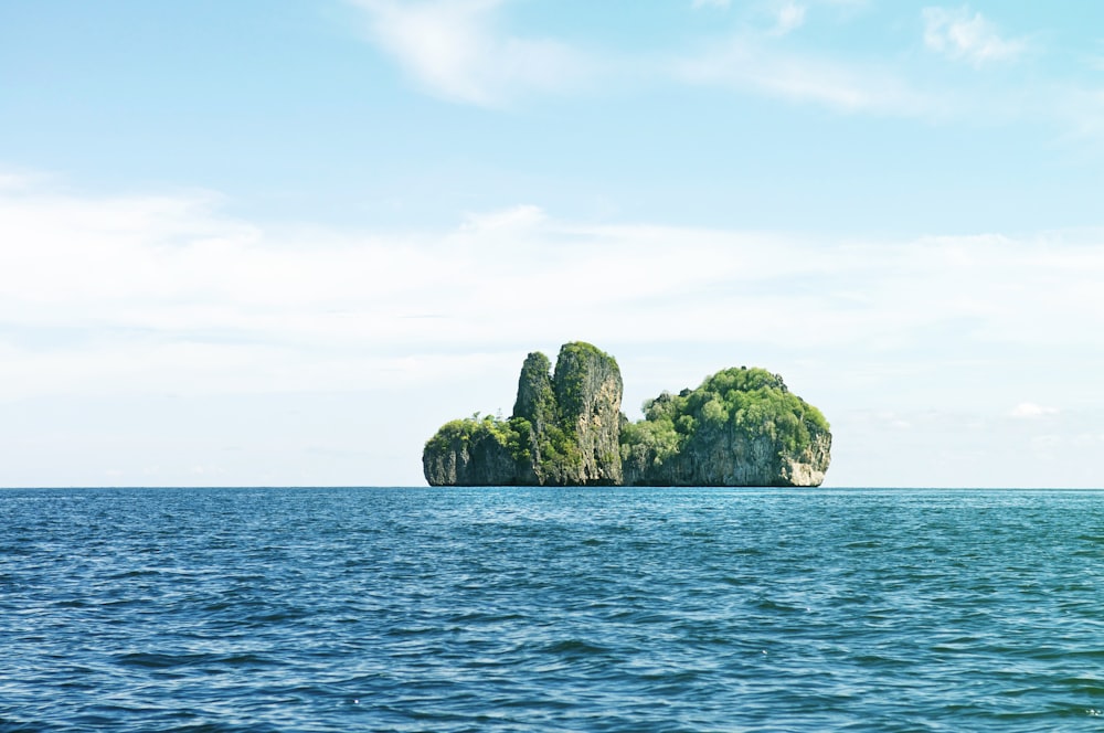 green and brown rock formation on blue sea under blue and white cloudy sky during daytime