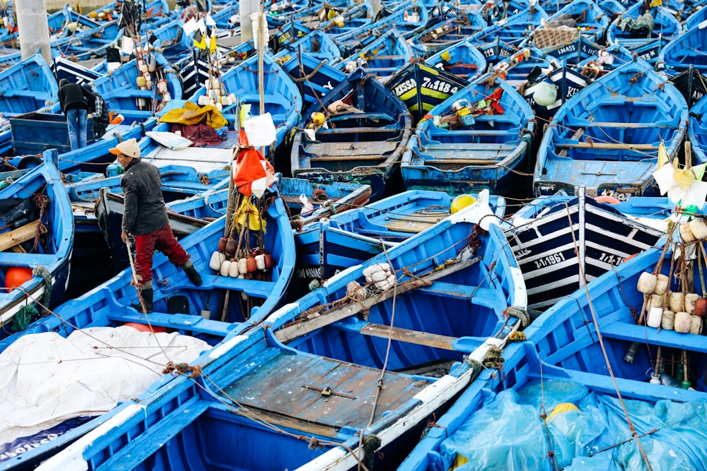 Hombre con chaqueta roja y jeans de mezclilla azul de pie en un barco azul y blanco durante el día